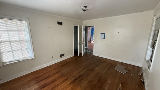 interior space featuring wood-type flooring, visible vents, crown molding, and baseboards