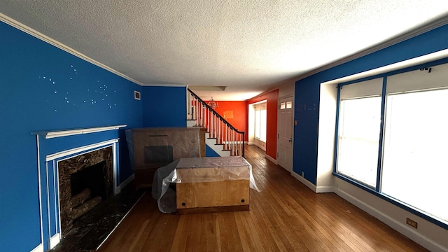 bedroom featuring a textured ceiling, a premium fireplace, baseboards, wood-type flooring, and crown molding