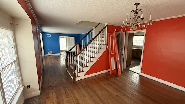 staircase featuring a textured ceiling, crown molding, baseboards, hardwood / wood-style floors, and an inviting chandelier