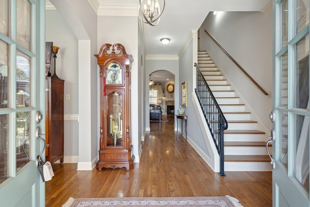 foyer entrance with arched walkways, ornamental molding, wood finished floors, baseboards, and stairs