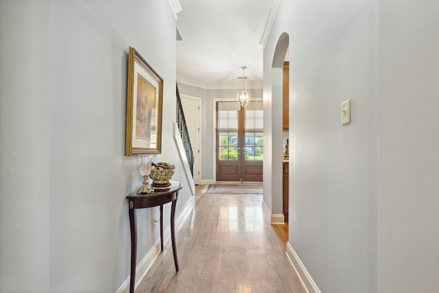 interior space with arched walkways, french doors, light wood-style flooring, ornamental molding, and baseboards