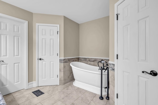 bathroom featuring tile patterned flooring, a freestanding tub, wainscoting, and tile walls