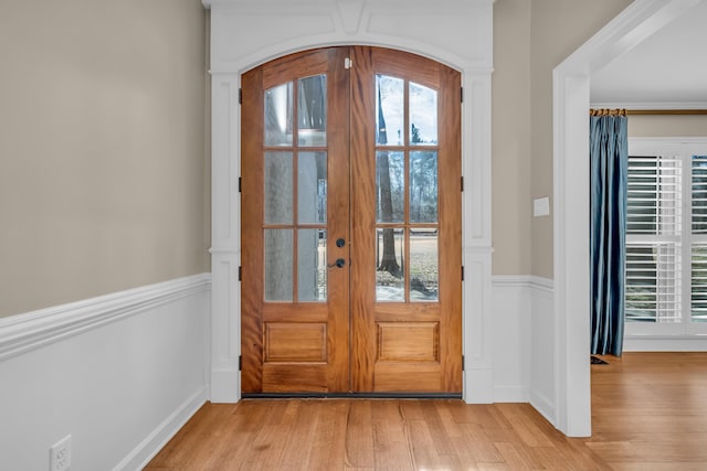 doorway featuring arched walkways, french doors, a wainscoted wall, and light wood-style floors