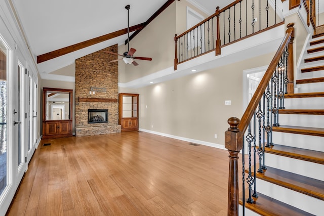 unfurnished living room featuring baseboards, visible vents, wood finished floors, a stone fireplace, and beam ceiling