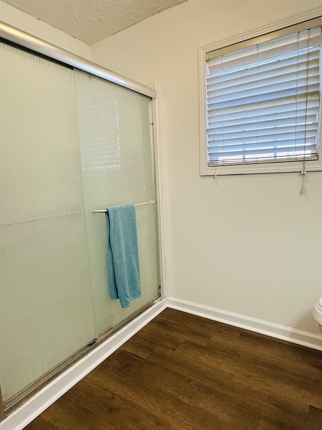 bathroom featuring a textured ceiling, wood finished floors, a shower with door, and baseboards