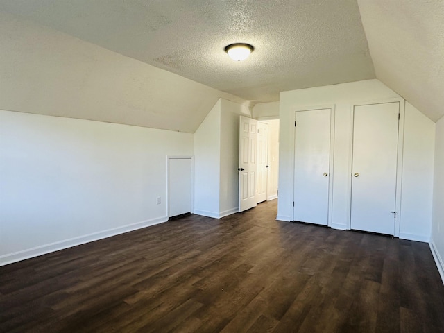 additional living space featuring lofted ceiling, baseboards, dark wood-style flooring, and a textured ceiling