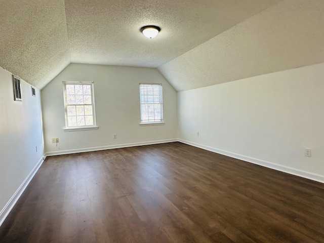 additional living space featuring a textured ceiling, dark wood finished floors, lofted ceiling, and baseboards