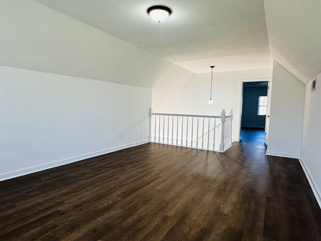 additional living space with lofted ceiling, a textured ceiling, dark wood-style floors, and baseboards