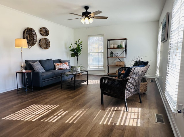 living area featuring dark wood-type flooring, visible vents, baseboards, and a ceiling fan