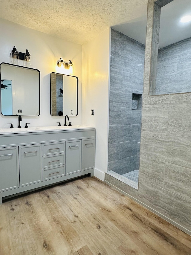 bathroom featuring double vanity, wood finished floors, and tiled shower