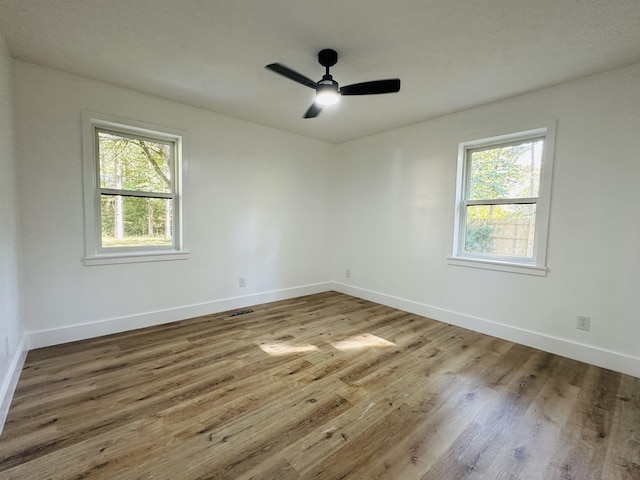 spare room with plenty of natural light, wood finished floors, visible vents, and baseboards