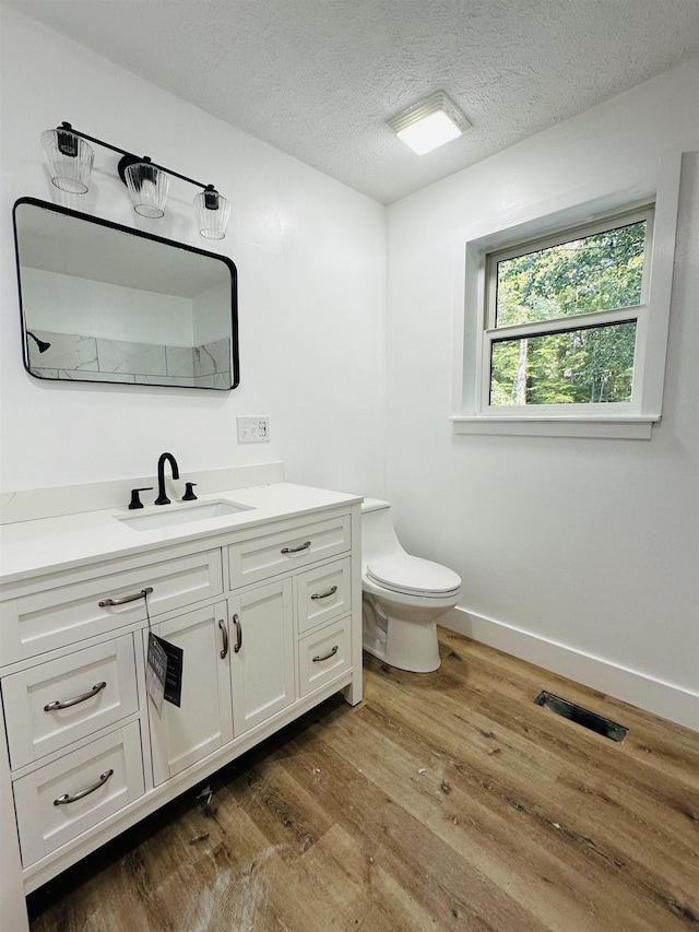 bathroom featuring visible vents, toilet, a textured ceiling, vanity, and wood finished floors