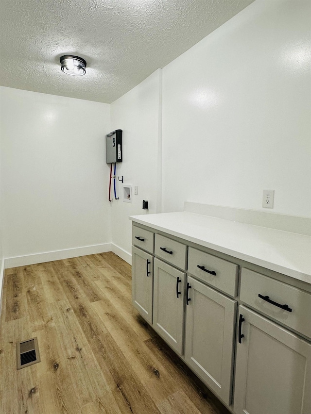 laundry room with a textured ceiling, washer hookup, visible vents, cabinet space, and light wood finished floors