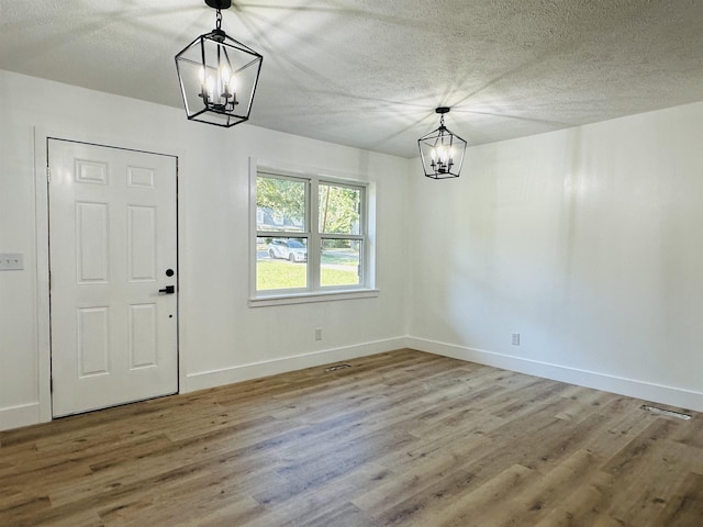 unfurnished dining area featuring a textured ceiling, a chandelier, and wood finished floors