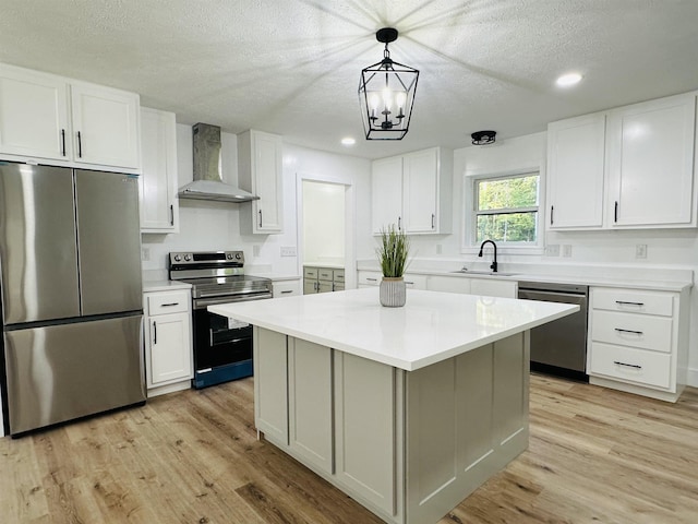 kitchen featuring wall chimney exhaust hood, appliances with stainless steel finishes, light wood-type flooring, white cabinetry, and a sink