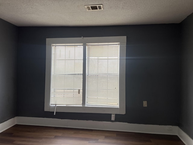 unfurnished room with a wealth of natural light, wood finished floors, visible vents, and baseboards