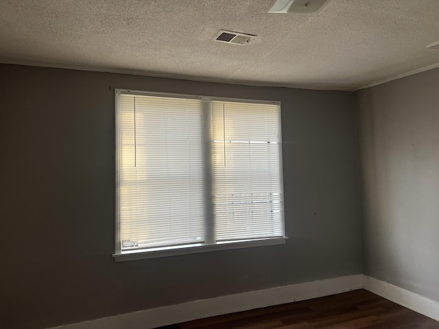 empty room featuring dark wood-style flooring, visible vents, a textured ceiling, and baseboards