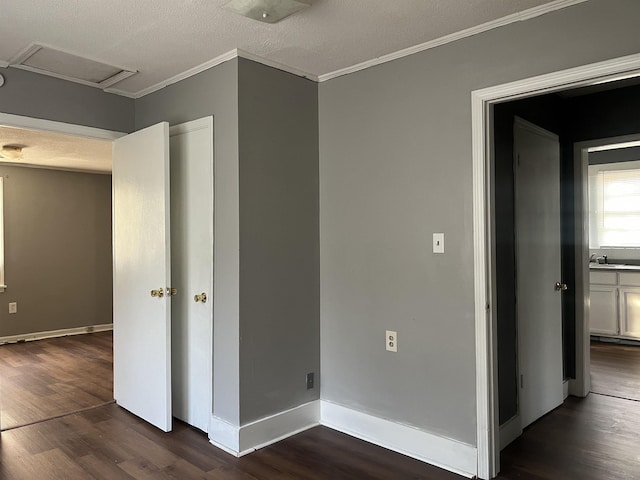 unfurnished bedroom with attic access, baseboards, ornamental molding, dark wood-style flooring, and a textured ceiling