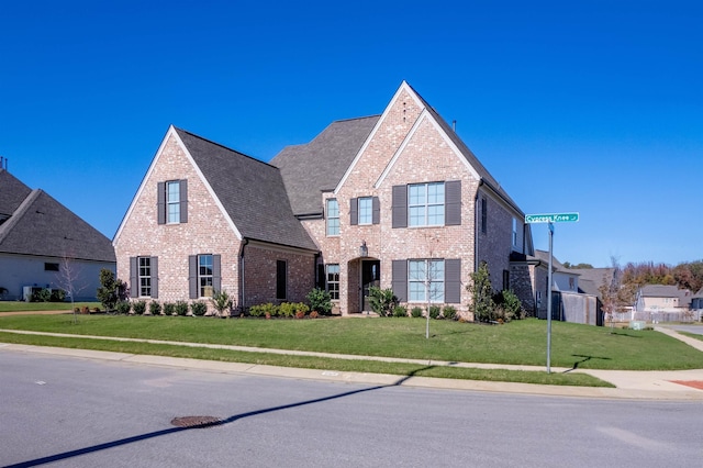 view of front of property with brick siding, a front lawn, and roof with shingles