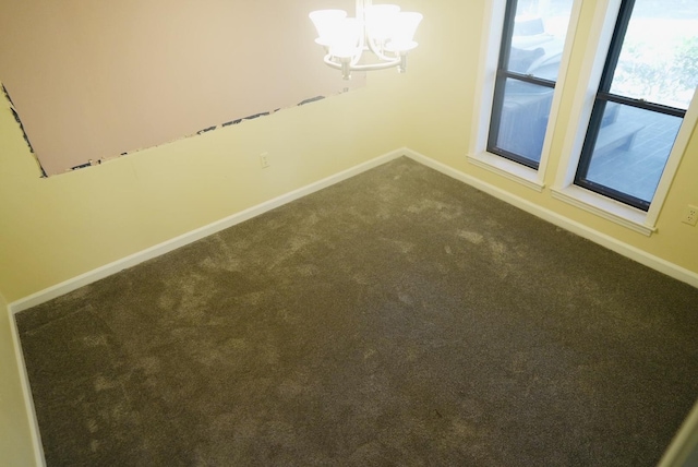 unfurnished room with a chandelier, dark colored carpet, and baseboards