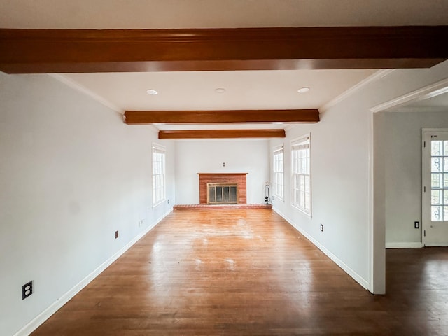 unfurnished living room with plenty of natural light, a fireplace, beamed ceiling, and wood finished floors