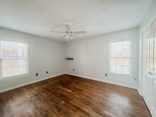 empty room with a healthy amount of sunlight, baseboards, and dark wood-type flooring