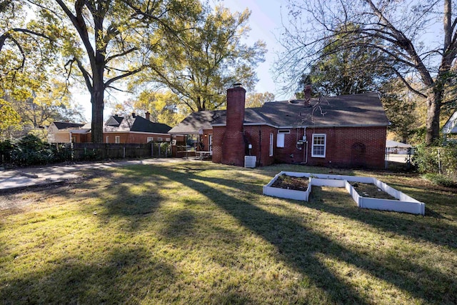 back of property with a vegetable garden, a chimney, fence, a yard, and brick siding