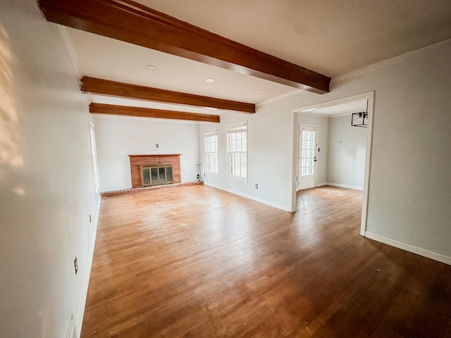 unfurnished living room with wood finished floors, baseboards, a brick fireplace, beam ceiling, and crown molding