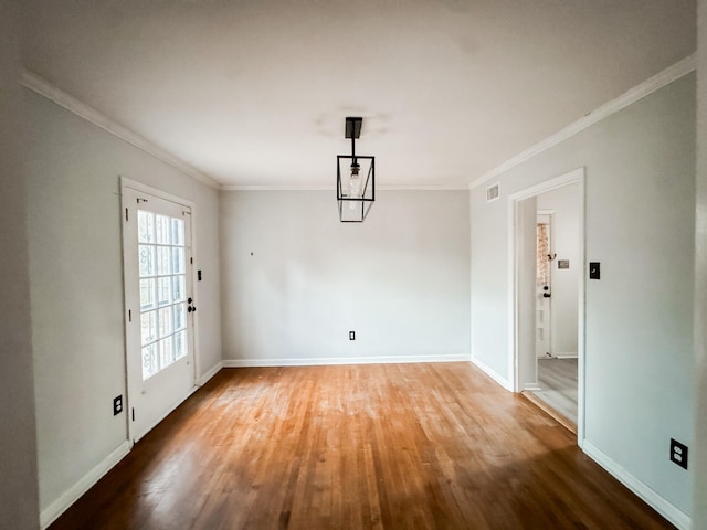 unfurnished dining area featuring baseboards, visible vents, wood finished floors, and ornamental molding