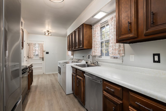 kitchen featuring washing machine and dryer, light wood-style flooring, stainless steel appliances, a sink, and light countertops