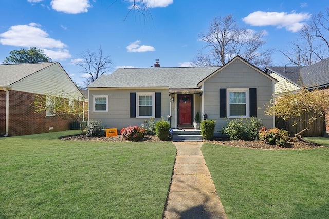 view of front of home with a shingled roof, a front yard, and fence