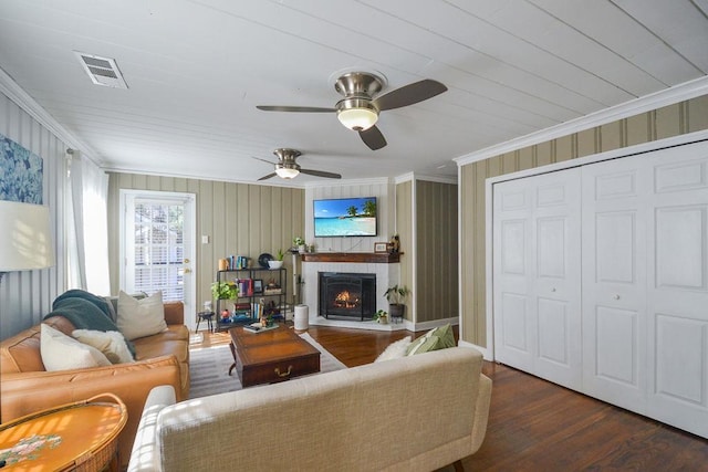 living room with a warm lit fireplace, visible vents, crown molding, and wood finished floors