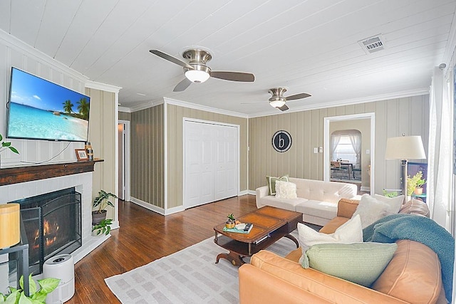 living room featuring a lit fireplace, wood finished floors, visible vents, and crown molding