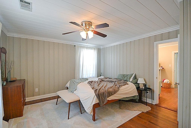 bedroom with ornamental molding, a ceiling fan, visible vents, and wood finished floors