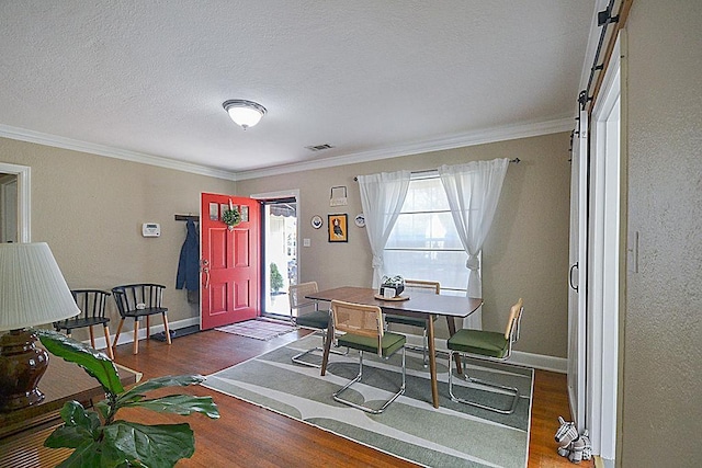 dining area featuring a barn door, wood finished floors, visible vents, baseboards, and crown molding