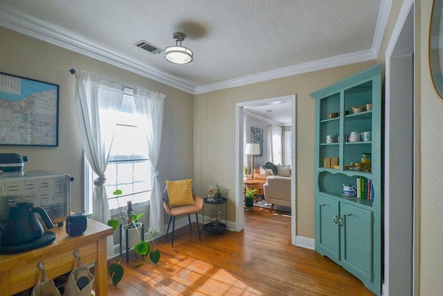 sitting room with plenty of natural light, visible vents, crown molding, and wood finished floors