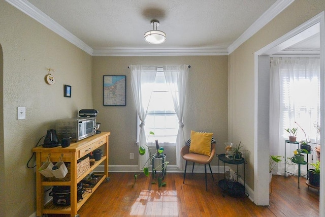 sitting room with ornamental molding, a textured wall, baseboards, and wood finished floors