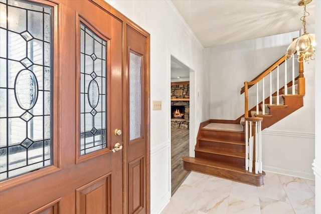 entryway featuring a stone fireplace, baseboards, marble finish floor, ornamental molding, and stairway