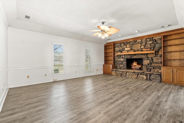 unfurnished living room with a textured ceiling, a stone fireplace, wood finished floors, visible vents, and built in features