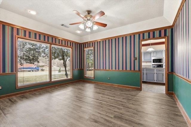 spare room with wood finished floors, a textured ceiling, and wallpapered walls