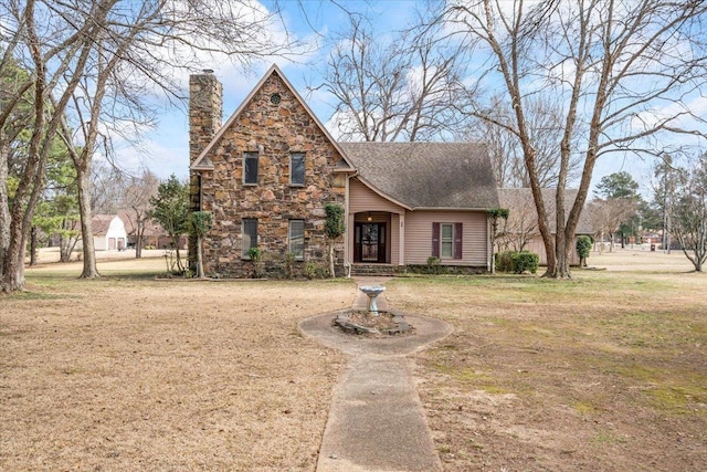 view of front of property featuring a shingled roof, stone siding, a chimney, and a front lawn