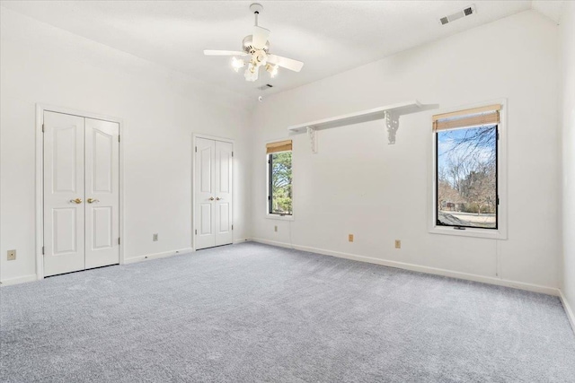 unfurnished bedroom with baseboards, visible vents, lofted ceiling, carpet flooring, and multiple closets