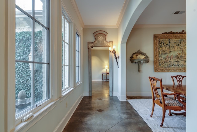 corridor featuring arched walkways, crown molding, visible vents, concrete flooring, and baseboards