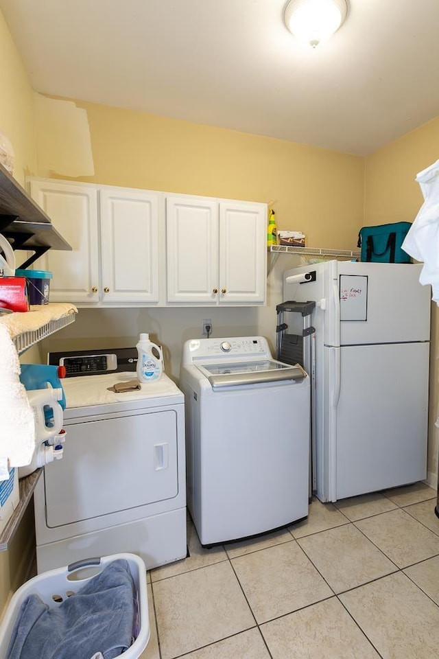 clothes washing area with light tile patterned floors, cabinet space, and washer and dryer