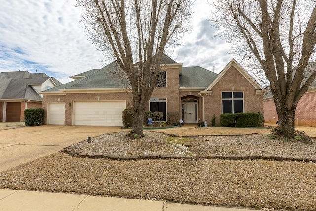 traditional home with a garage, driveway, a shingled roof, and brick siding