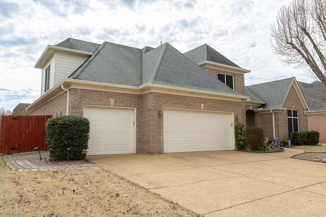 view of side of home with an attached garage, roof with shingles, concrete driveway, and brick siding