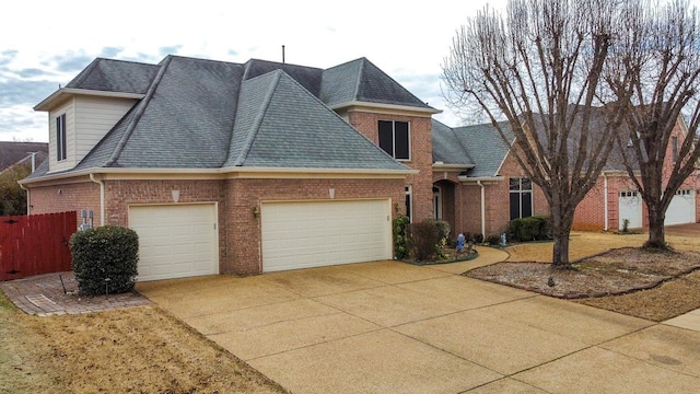 view of front of home with brick siding, a shingled roof, an attached garage, fence, and driveway