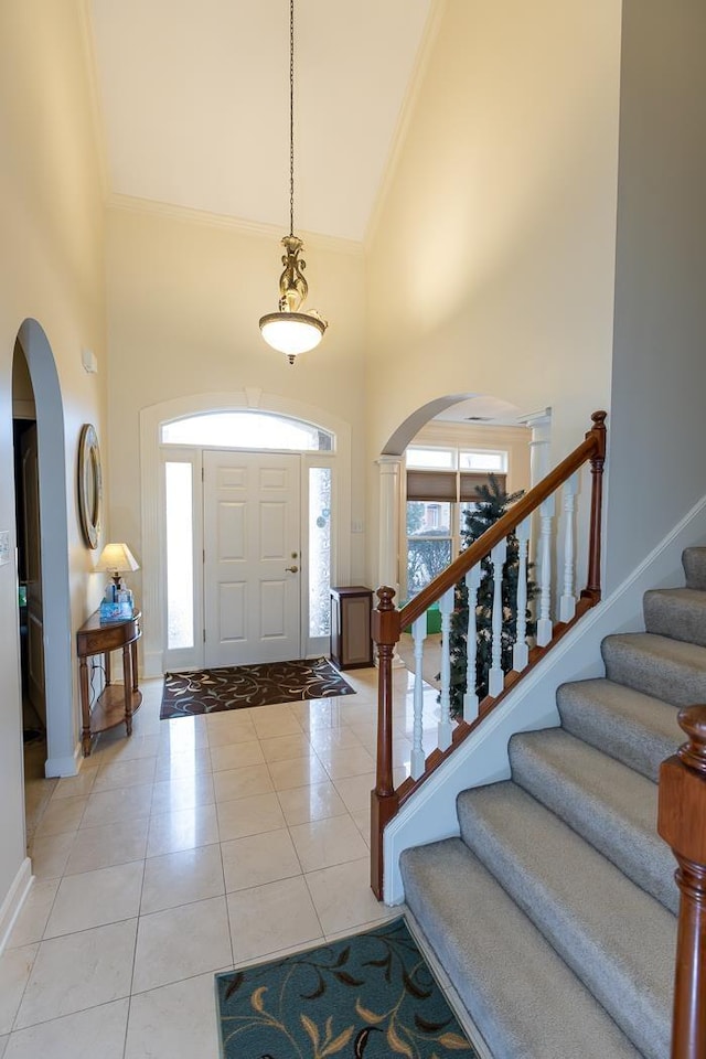 entrance foyer featuring arched walkways, crown molding, a high ceiling, and light tile patterned floors