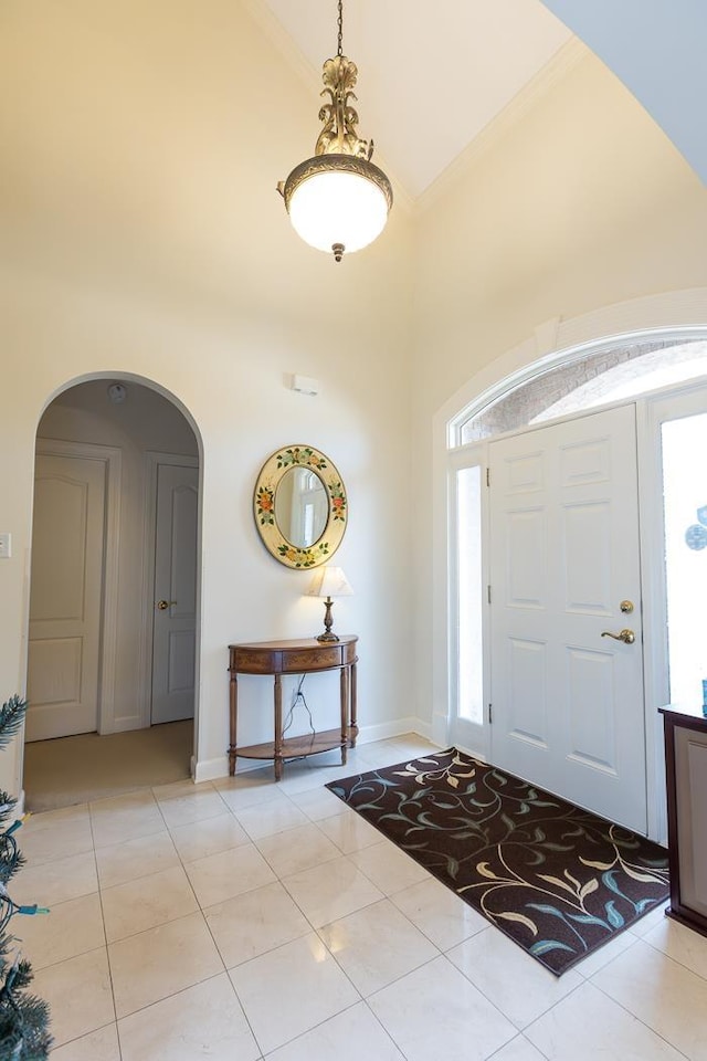 foyer with ornamental molding, arched walkways, a high ceiling, and light tile patterned floors