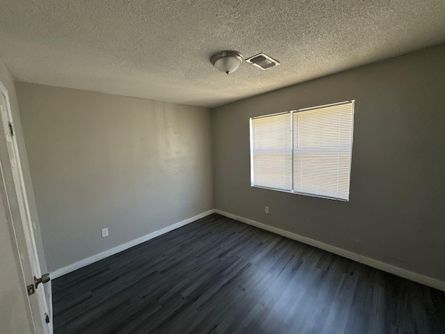 unfurnished room featuring visible vents, dark wood finished floors, a textured ceiling, and baseboards